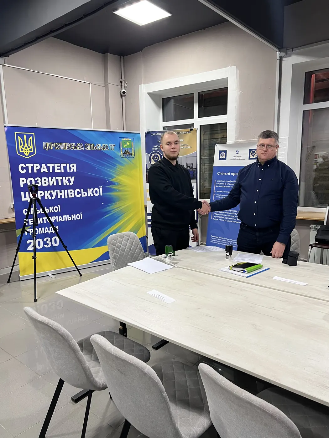 Двоє чоловіків тиснуть руки в залі; позаду — ролап «Стратегія розвитку Циркунівської сільської територіальної громади 2030» і банер Навчально-наукового інституту «Інститут державного управління» ХНУ імені В. Н. Каразіна