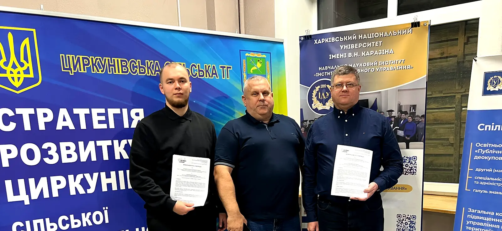Троє учасників із примірниками меморандуму на тлі ролапу Циркунівської громади та стенда Інституту державного управління