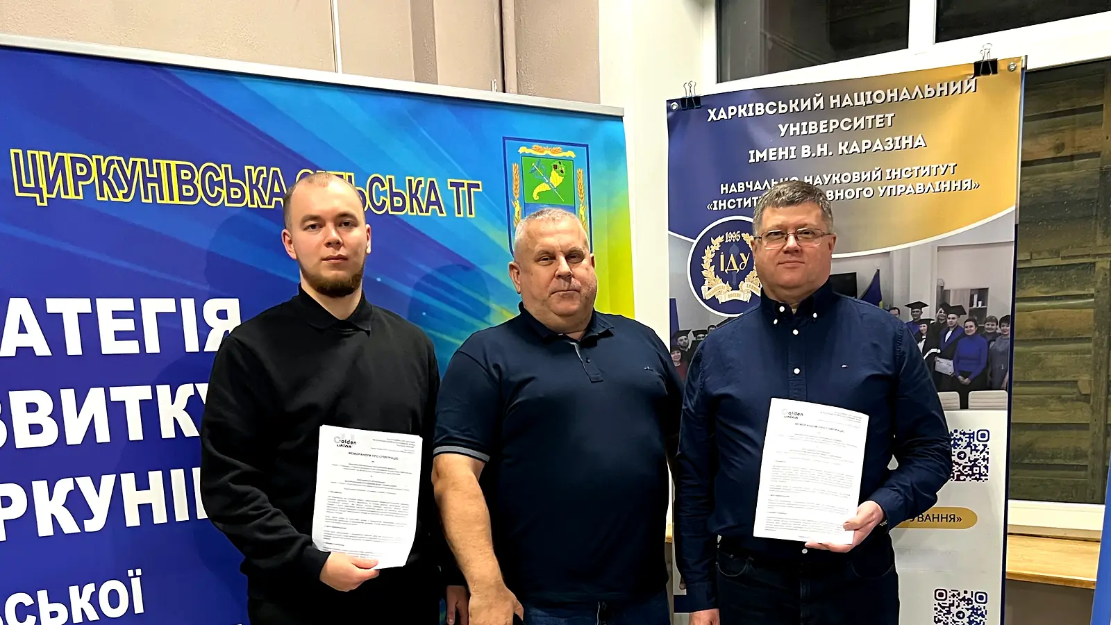 Троє учасників із примірниками меморандуму на тлі ролапу Циркунівської громади та стенда Інституту державного управління
