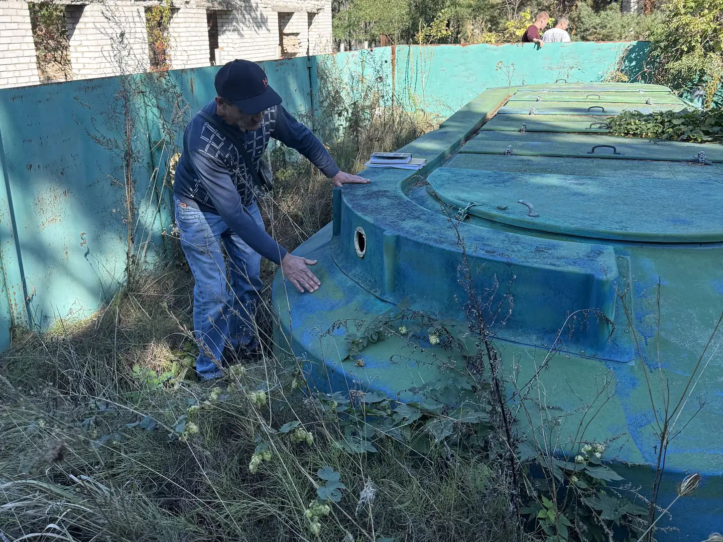 Чоловік оглядає бірюзову бетонну споруду серед високої трави