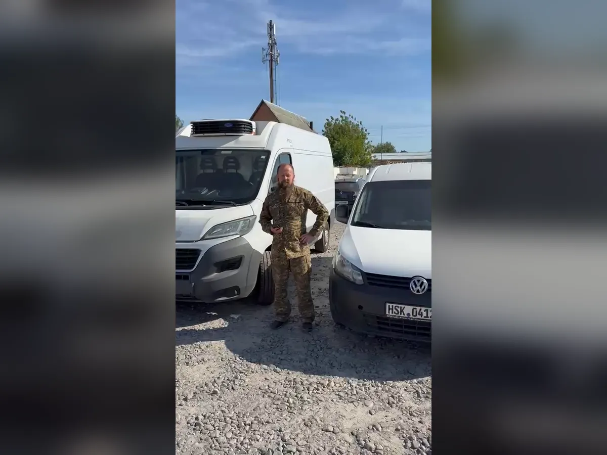 Військовий у формі стоїть між білими фургонами-рефрижераторами Fiat Ducato і Volkswagen Caddy на гравійному майданчику, кадр із відеоподяки