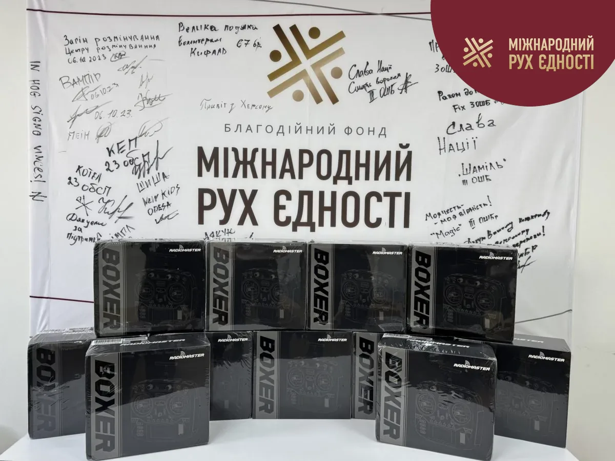 Одинадцять коробок з пультами керування дронами RadioMaster Boxer на тлі банера благодійного фонду «Міжнародний Рух Єдності» з подяками від підрозділів