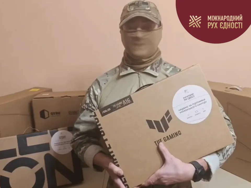 Військовослужбовець полку безпілотних систем «Кракен 1654» у балаклаві тримає коробку ноутбука Asus TUF Gaming A16 з наліпкою фонду, кадр із відеоподяки