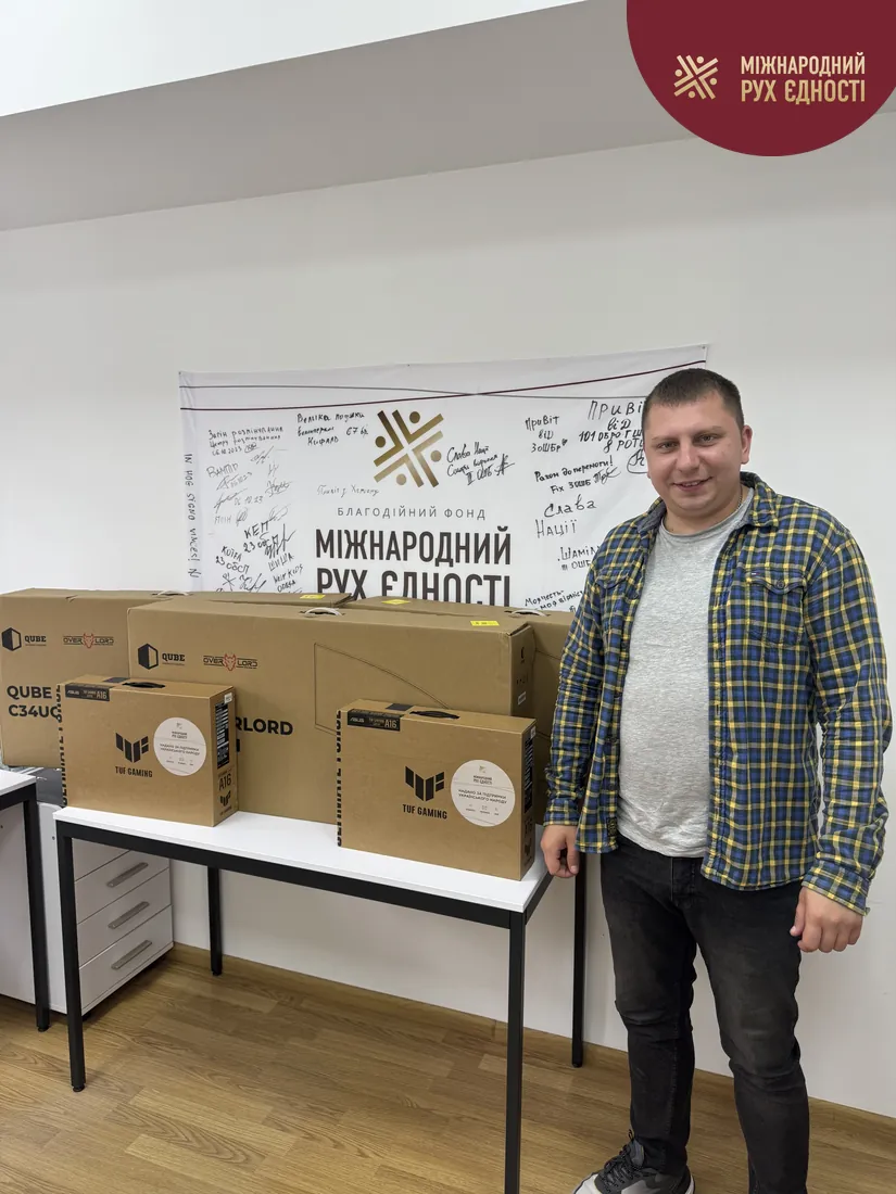 Працівник фонду «Міжнародний Рух Єдності» поруч із двома ноутбуками Asus TUF Gaming A16 і трьома моніторами QUBE Overlord перед передачею полку «Кракен 1654»